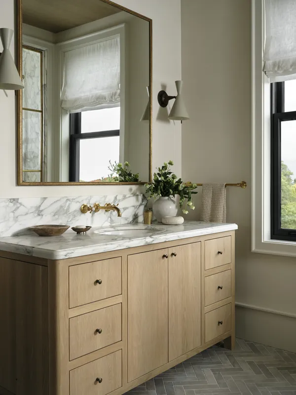 Farmhouse bathroom with an oak vanity, marble top and herringbone tile floor