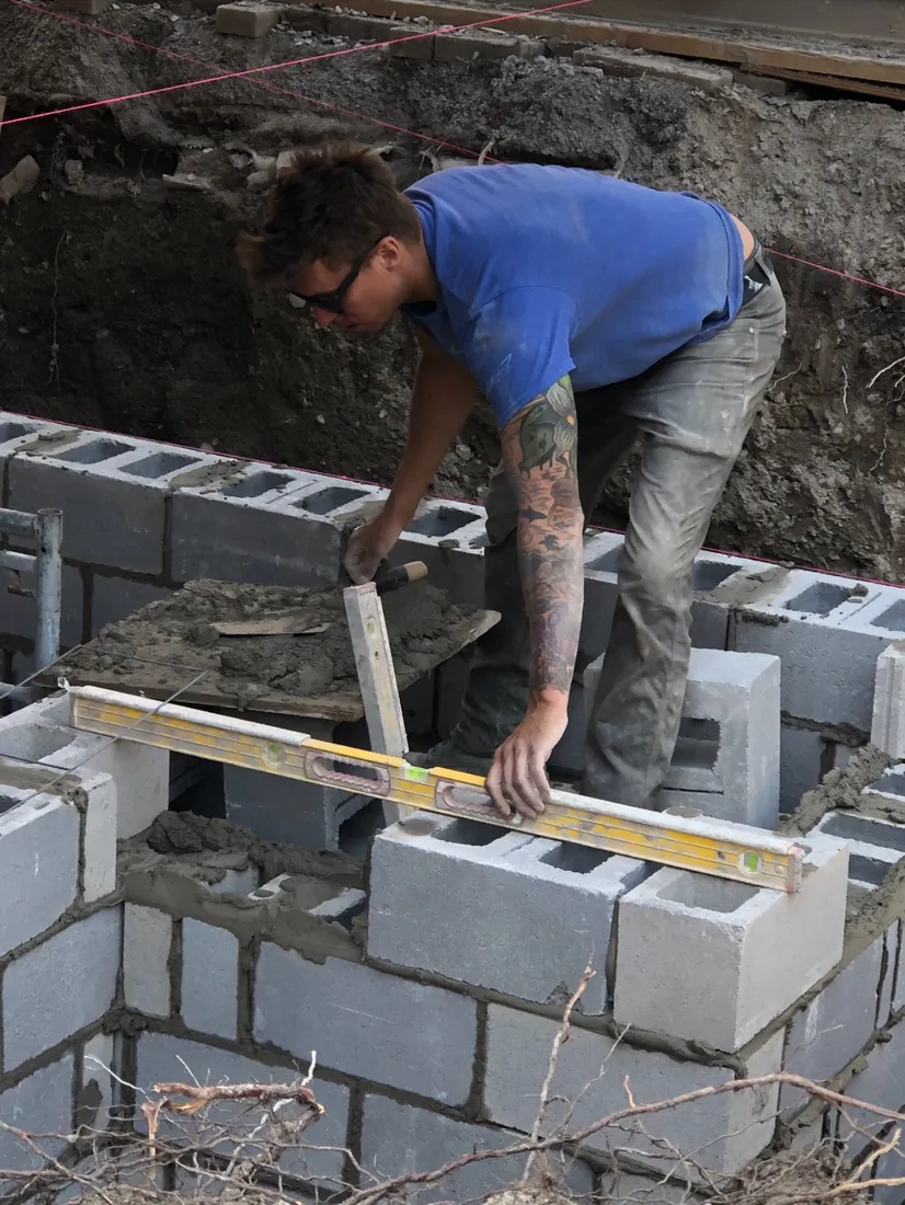 A Strongback mason levelling a course of concrete block on site