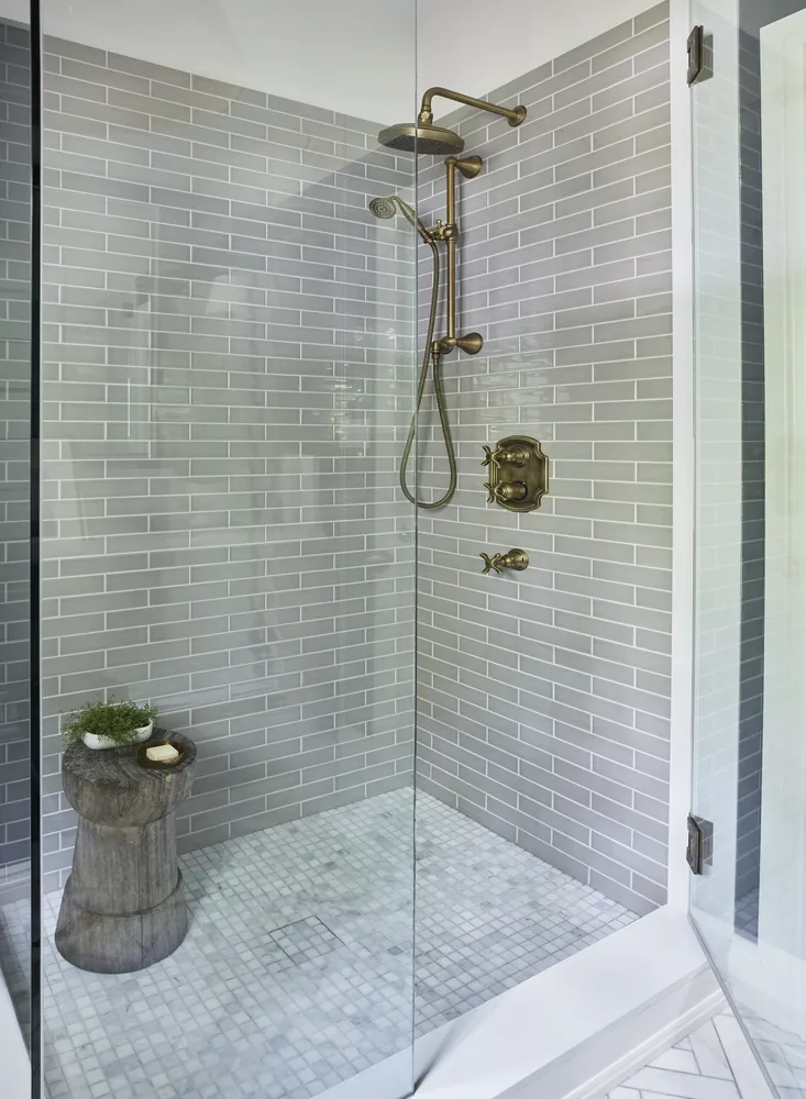 Grey tiled walk in shower with a marble mosaic floor and brass fixtures